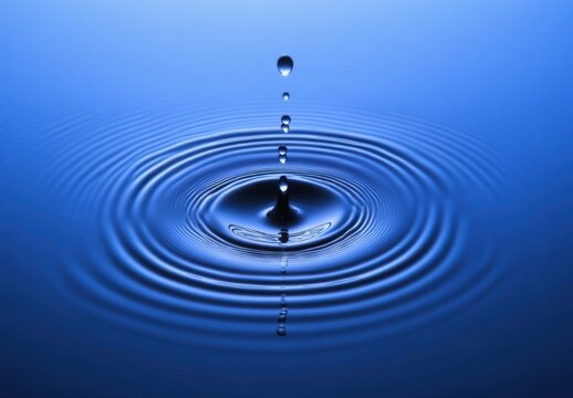 A water drop falling into blue water, creating ripples and waves.