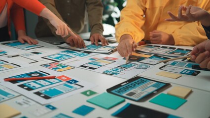 A diverse team collaborates during a design session, pointing at mobile app wireframes and sketches...