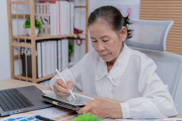 A senior woman using a digital tablet and stylus in a modern office setting, focused on her work.