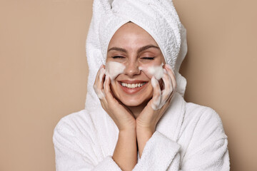 Beautiful woman washing her face with cleansing foam on beige background