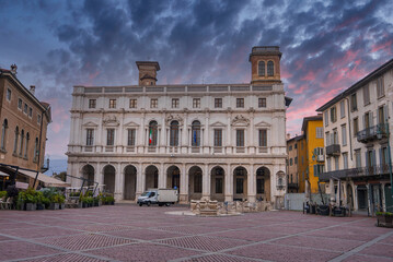 Fototapeta premium Piazza Vecchia in Bergamo, Italy, features the Renaissance style Palazzo Nuovo, a fountain, historic buildings, and a colorful sunset sky.