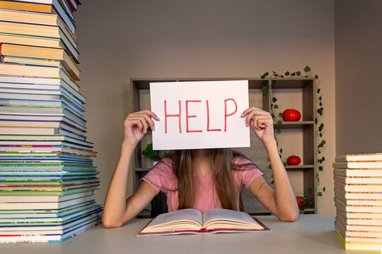 Overwhelmed student holding help sign behind desk.