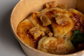 Fried dumplings with golden crust and crispy pork cracklings in a kraft paper bowl. Traditional Eastern European food, close-up, delicious street food concept