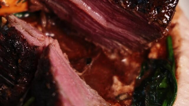 close up of filet mignon beef meat in plate and someone cutting with knife a piece. tasty sauce and cream with fried spinach.medium rare preparation of meat, juicy middle.