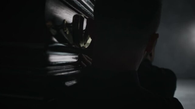 Back view close-up shot of four men carrying dark wooden coffin during grim funeral procession