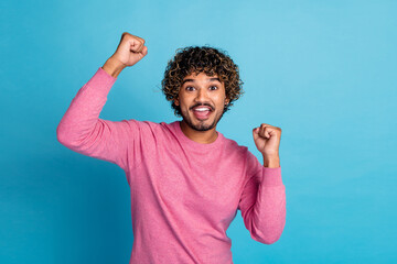 Energetic Young Man in Pink Sweater Celebrating with Raised Fists on Vibrant Blue Background