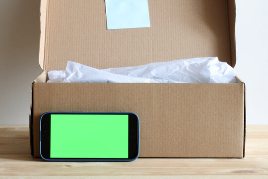 Smartphone with green screen leaning on open cardboard box with tissue paper