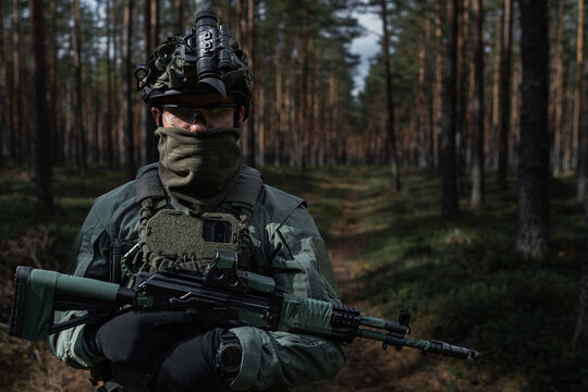Special forces soldier in gear, helmet with NVG, and rifle equipped with a red dot sight in the forest.
