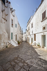 Scenic view of Ostuni, Italy's 'White City,' showcasing whitewashed buildings under a clear blue sky, with narrow streets and historic architecture illuminated by sunlight.