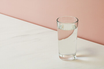 Glass of fresh water on white table with pink background