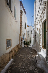 Scenic view of Ostuni, Italy's 'White City,' showcasing whitewashed buildings under a clear blue sky, with narrow streets and historic architecture illuminated by sunlight.
