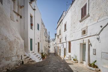 Scenic view of Ostuni, Italy's 'White City,' showcasing whitewashed buildings under a clear blue sky, with narrow streets and historic architecture illuminated by sunlight.