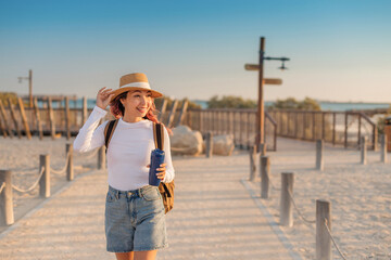 Female tourist holding a reusable water bottle and walking on a boardwalk in Park on Hudayriyat...