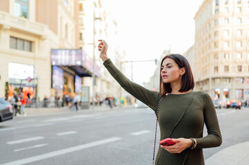 Businesswoman hailing taxi cab in Madrid city center holding smartphone