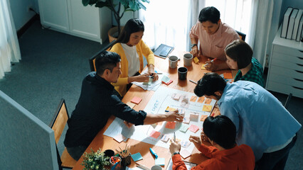 Top down view of diverse people brainstorming and making scrum task board. Group of skilled business team working together and writing sticky notes to share plan and using kanban board. Convocation.