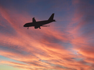 Silhouette of a holiday jet with wheels down to land at its destination airport to land isolated against a dramatic sunset sky. Copy space. Travel concept.