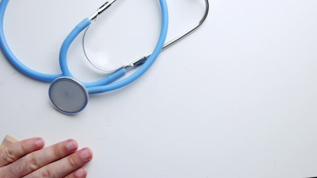 patient giving bribery to doctor. hand putting in pocket some money or putting on the table. corruption problem in medical system, stethoscope close up, medical assistant looking on bancnote.
