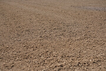 A close-up of tilled soil or a dirt surface, the texture is rough and uneven, with small clumps and particles visible