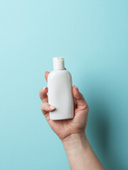 Cosmetic bottle in woman hand on blue background.