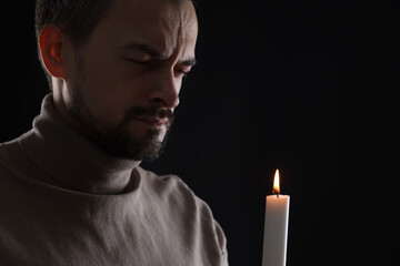 Sad man with burning candle crying on black background, space for text