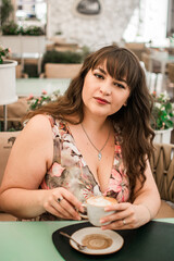 Young plus size woman with long hair sitting with a cup of coffee
