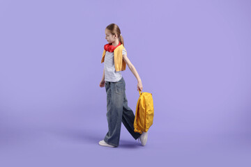 Stylish schoolgirl with backpack and headphones on violet background