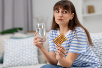Woman with contraceptive pills and glass of water on sofa at home. Space for text