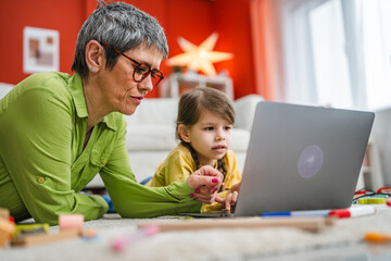 Obraz premium grandmother and grandchild lying down on floor and use laptop together