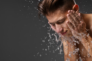 Handsome man washing his face on grey background. Space for text