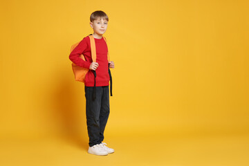 Cute schoolboy with backpack on orange background, space for text