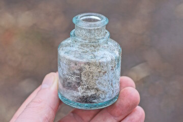 one hand holds old small dirty gray glass jar on autumn street