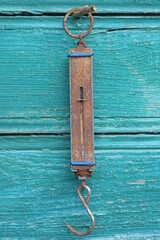 one old long brown iron canter scale in rust hanging on green wooden wall outside