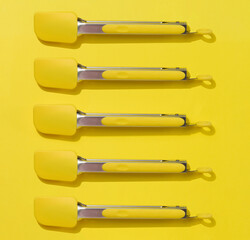 Yellow kitchen tongs with shadow on yellow background, top view