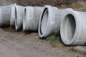A row of large concrete pipes lying on a dirt road. Industrial construction material, urban...