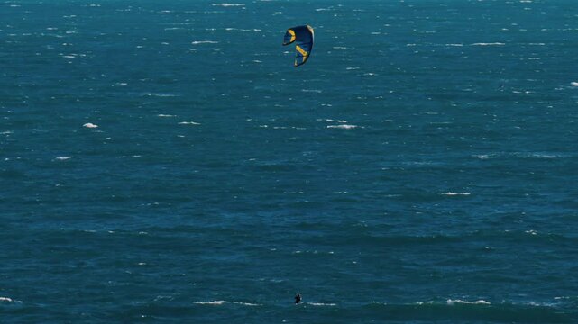 Distant view of a man kitesurfing on a sunny day