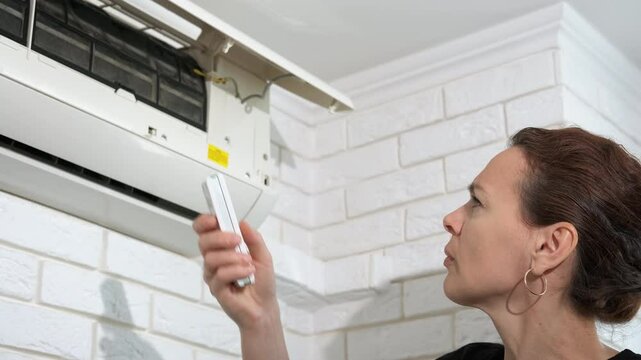 Woman switch the broken conditioner. A view of stressed female with remote controller try to switch the conditioner in the room.