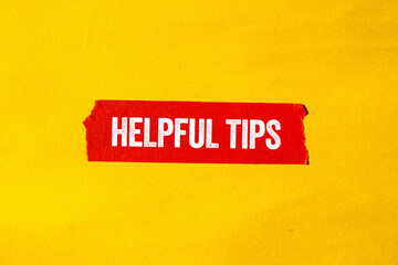 Helpful tips message written on ripped torn red paper tape on yellow background. Conceptual helpful tips symbol. Copy space.