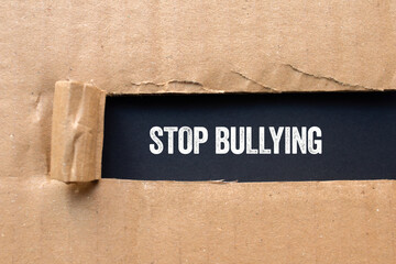 Stop bullying message written on ripped torn cardboard paper on black background. Conceptual stop...