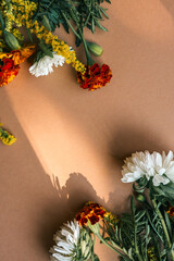 Flat lay composition of white chrysanthemums, orange marigolds, and yellow goldenrods on a warm...
