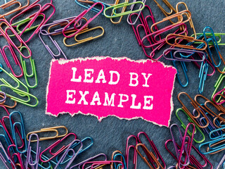 Lead by example message written on ripped torn pink paper piece on grey background. Conceptual lead...