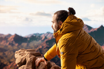 Fototapeta premium Male hiker looks out over a breathtaking mountain range from the hill top, embracing the solitude and fresh air of the great outdoors. Sense of adventure and endless nature exploration.