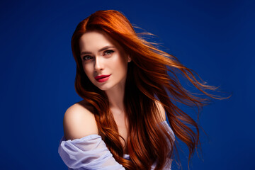 Fototapeta premium Portrait of a young female with red hair in a studio setting against a vibrant blue background
