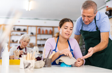 elderly man potter teaches young girl to make clay products