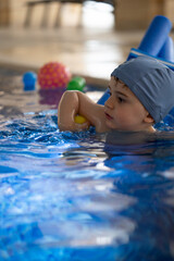 Obraz premium Child swimming with floatation device and balls in pool