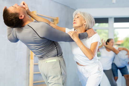 Purposeful mature female pupil clash with training manager during Krav Maga self-defense lesson, repulse charge, intensity of practice. Martial arts school, melee - Powered by Adobe