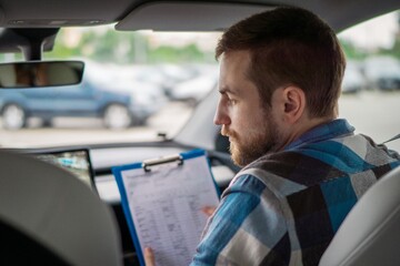 Instructor holding drive test report while sitting on the passenger seat. Back view. Driving test,...