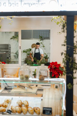 General view of a small business with the chef preparing food in the background, surrounded by plants and pastries. Plenty of foreground copy-space. Vertical.
