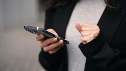 Caucasian female standing outdoors around grey modern buildings, working on her phone, smiling,...