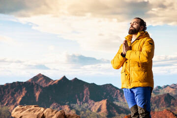 Pleased calm nature lover meditating on top of the mountain range, doing meditation poses and...