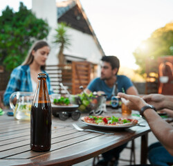 Bottle, alcohol and friends in garden for dinner, lunch and bonding together with meal outdoor. Social gathering, people and beverage with food, healthy salad or hungry with nutrition for celebration